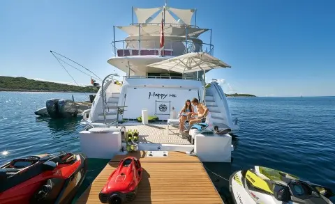 Happy Me yacht docked with people on a wooden pier and small boats nearby