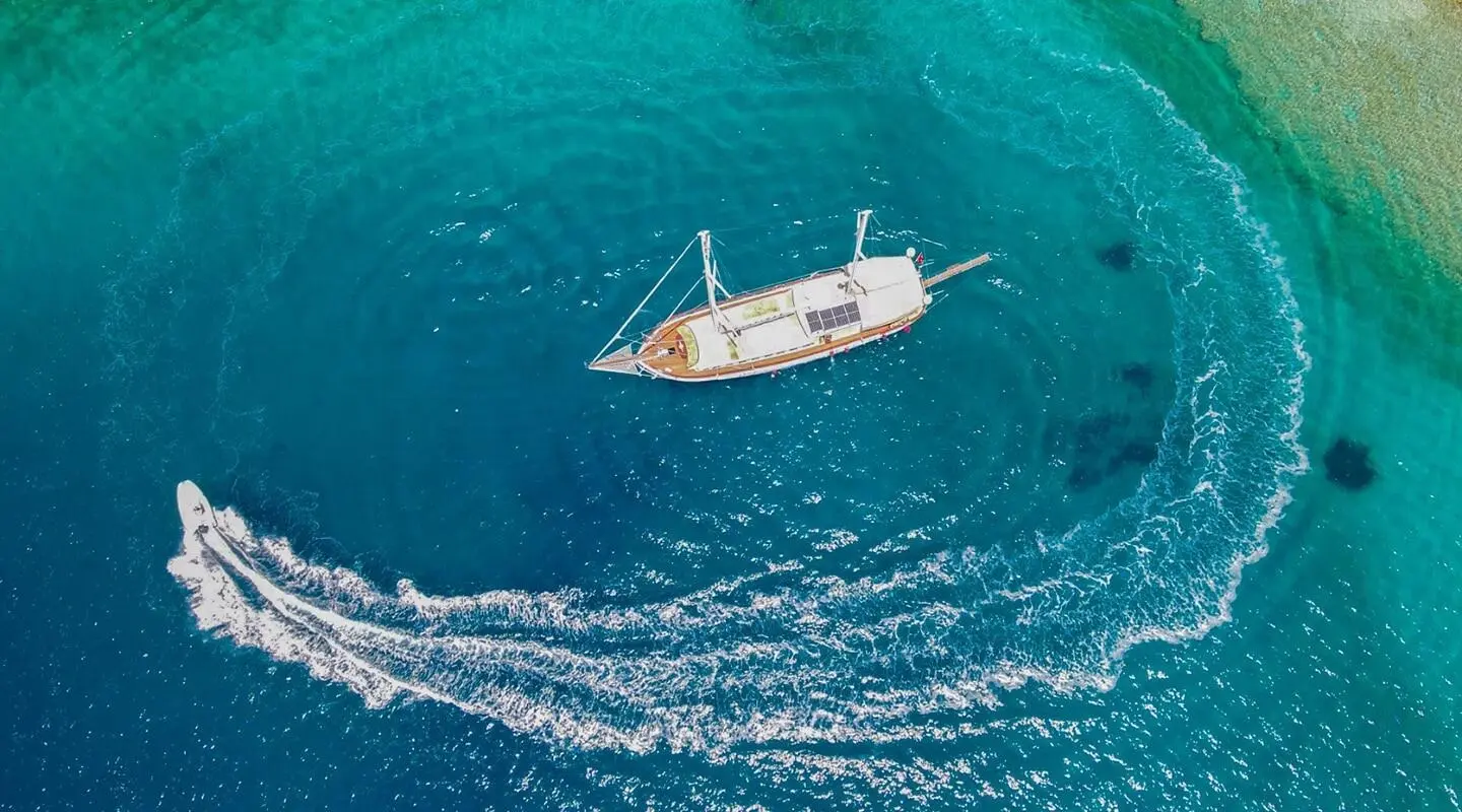 Small white yacht Ulucinar anchored in turquoise sea, aerial view at sunset