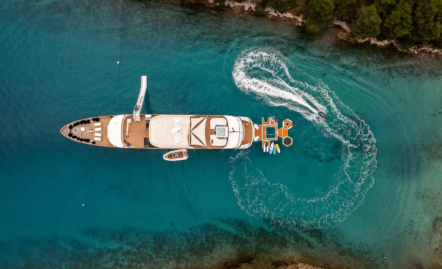 A white motor yacht named Cristal anchored in turquoise sea, aerial view
