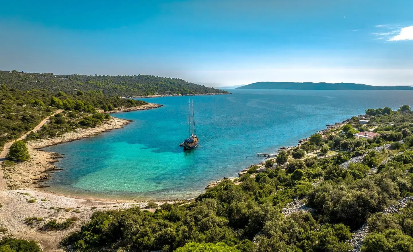 A luxury gulet yacht anchored near a turquoise bay with rugged coastline.