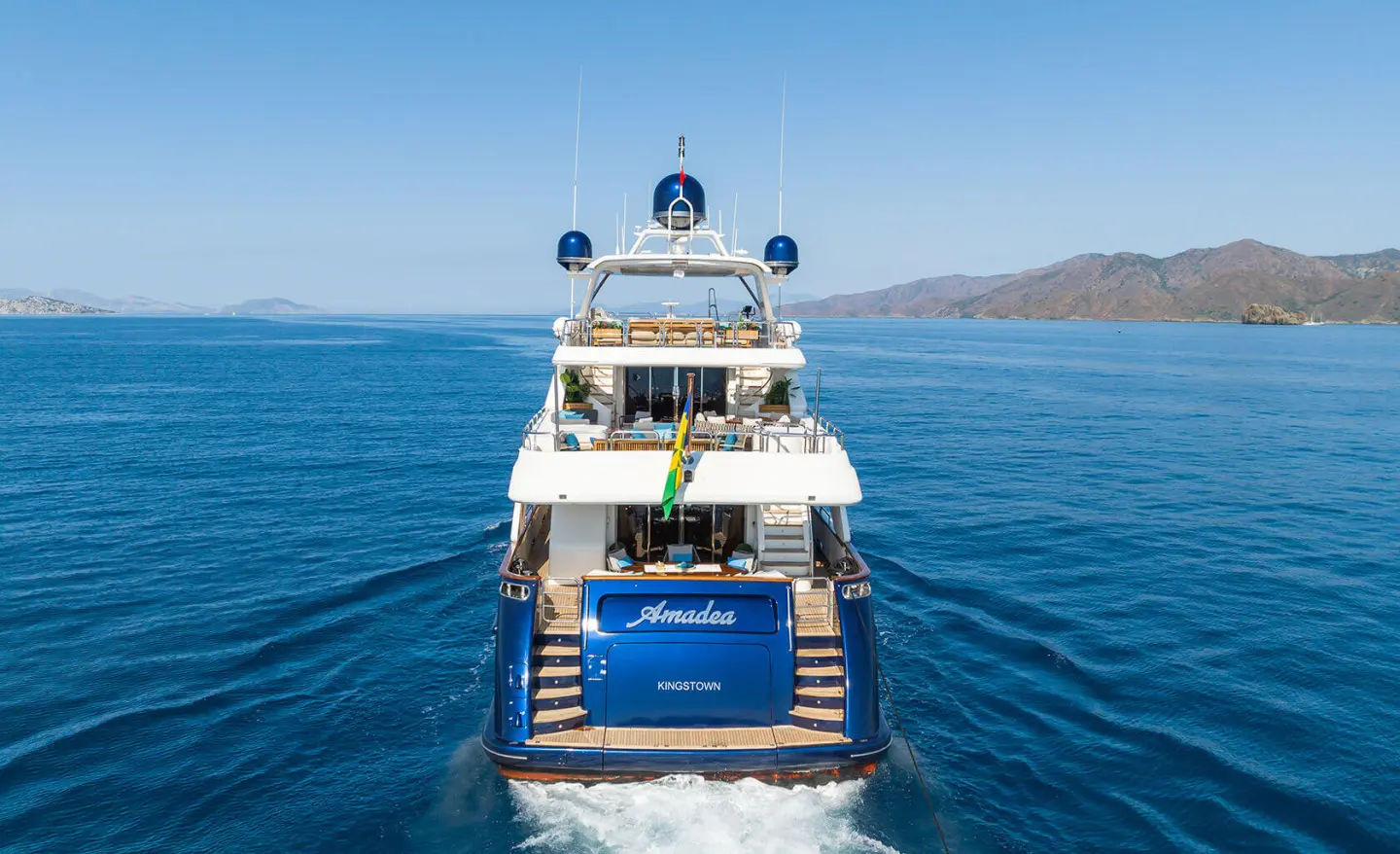 Amadea yacht cruising on blue sea, rear deck view with upper deck and wake