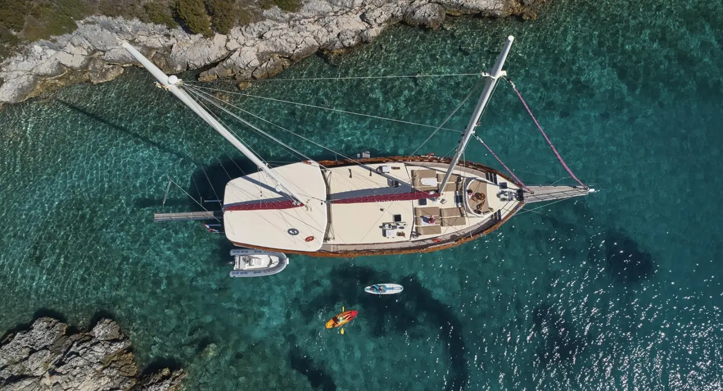 Gulet yacht anchored near rocky coastline with deck and clear blue water