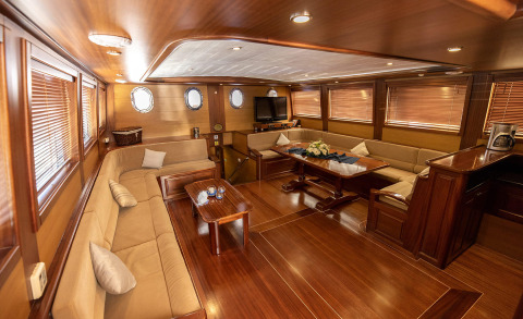 Interior of Kayhan 4 gulet saloon with wooden walls, L-shaped beige sofas and a central table