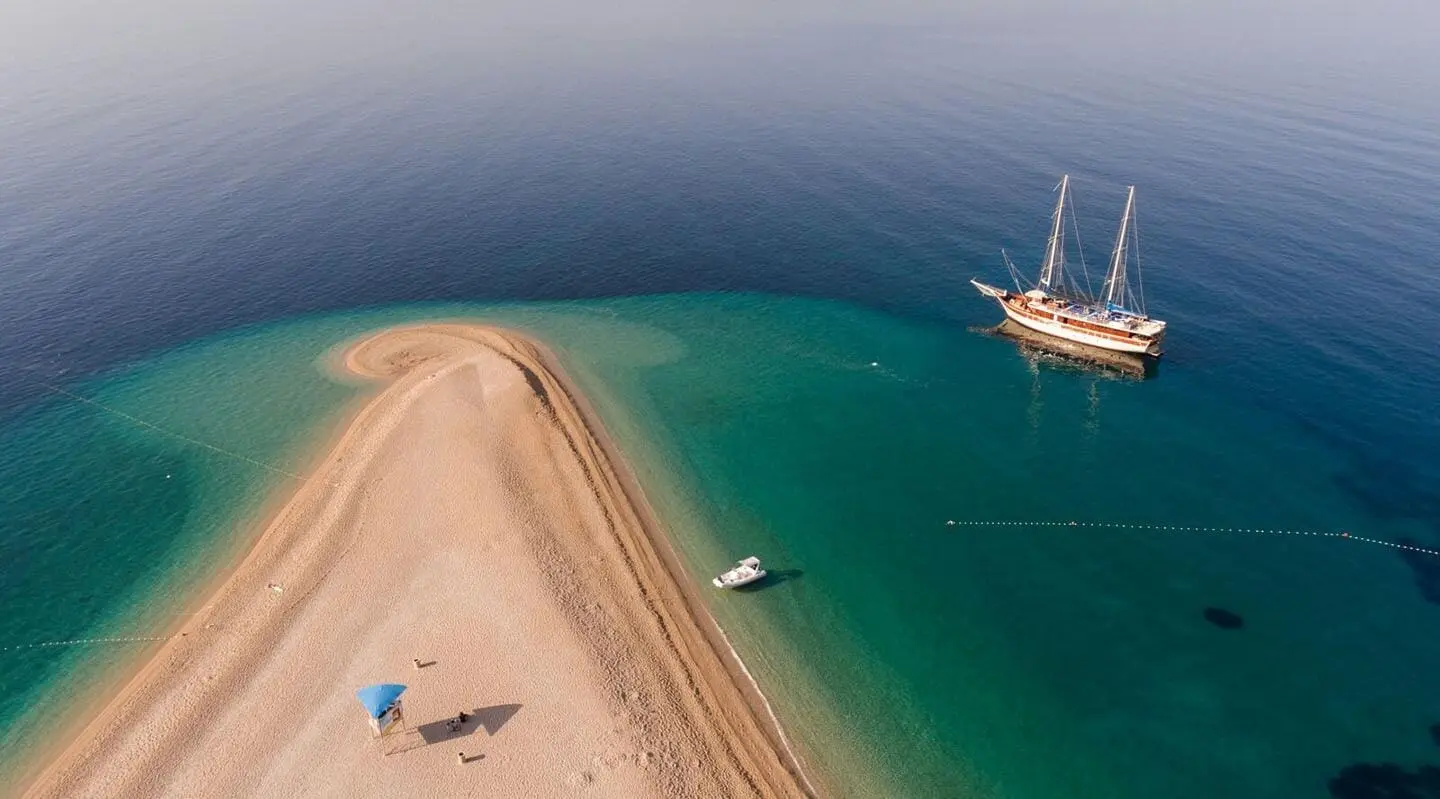 Tajna Mora yacht anchored near a sandy beach at sunset, turquoise water