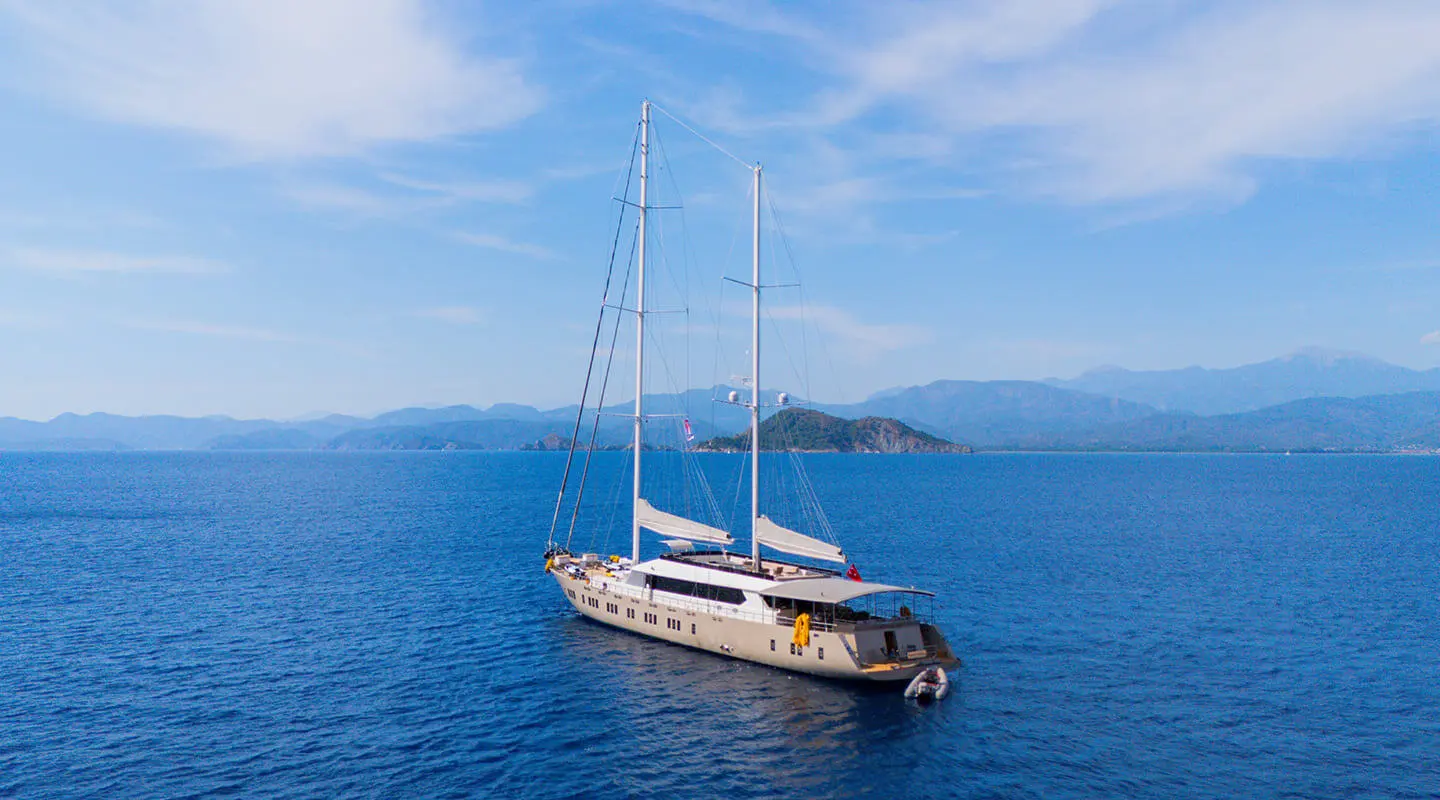 Yacht named King Of The Sea anchored on blue sea with mountains in background
