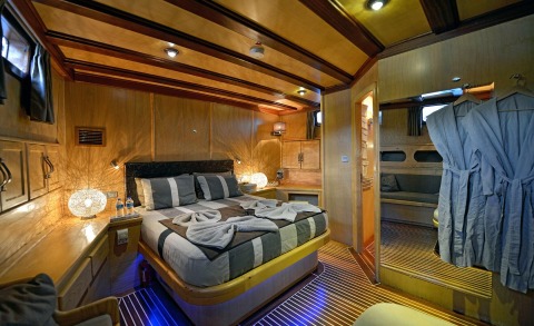 Wood-paneled cabin with a large bed, bedside lamps, and wooden ceiling beams