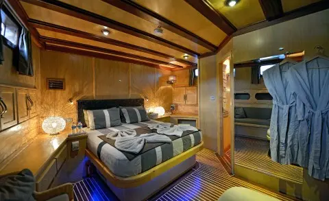 Interior of gulet Derin Deniz master cabin with bed, wooden beams, and warm lighting