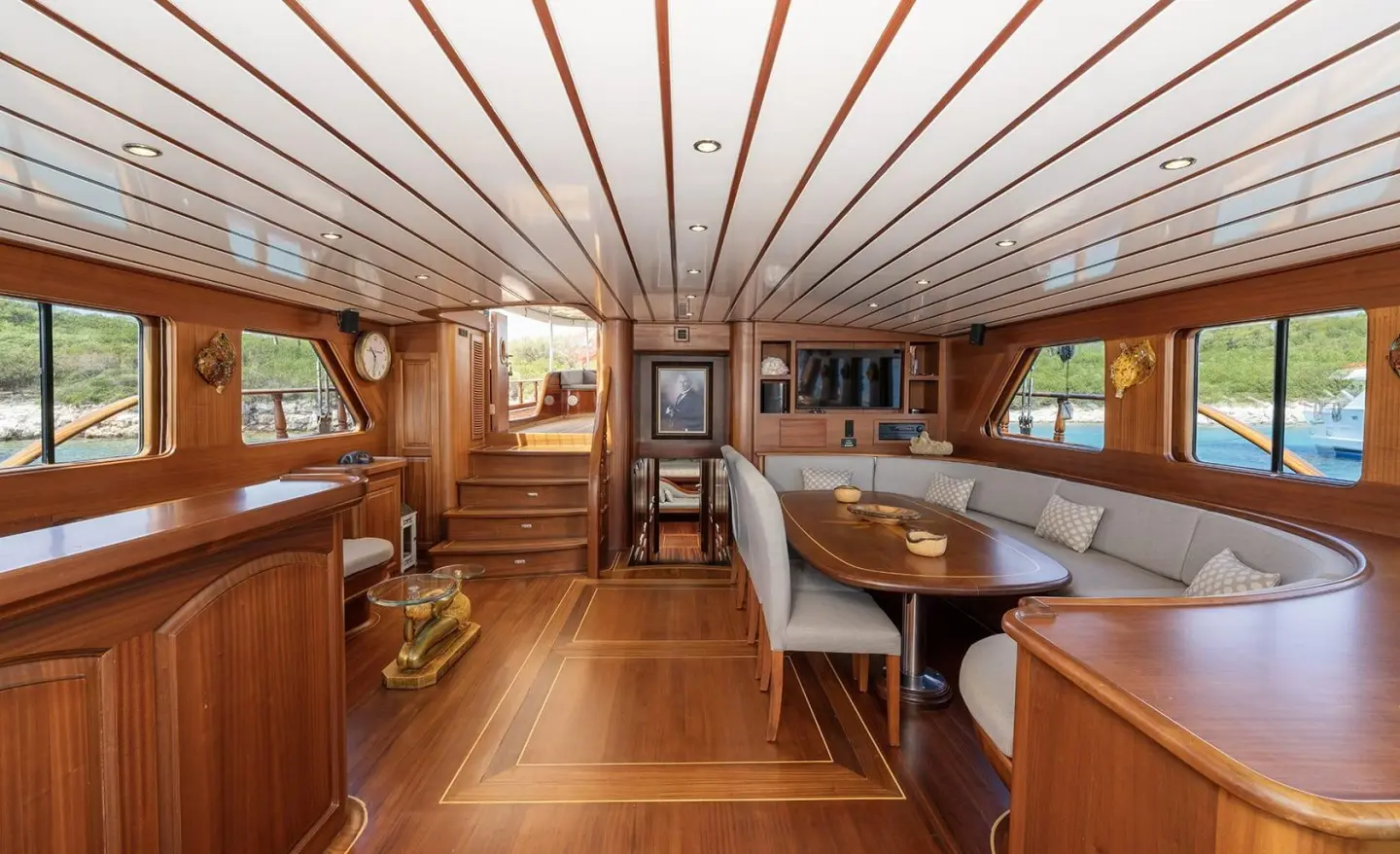 Interior of a yacht with polished wooden deck, table and seating under a curved skylight