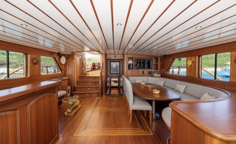 Interior of a luxury gulet yacht with wooden panels, curved seating around a table, and built-in cabinetry