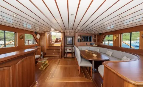 Interior of a yacht with polished wooden deck, table and seating under a curved skylight