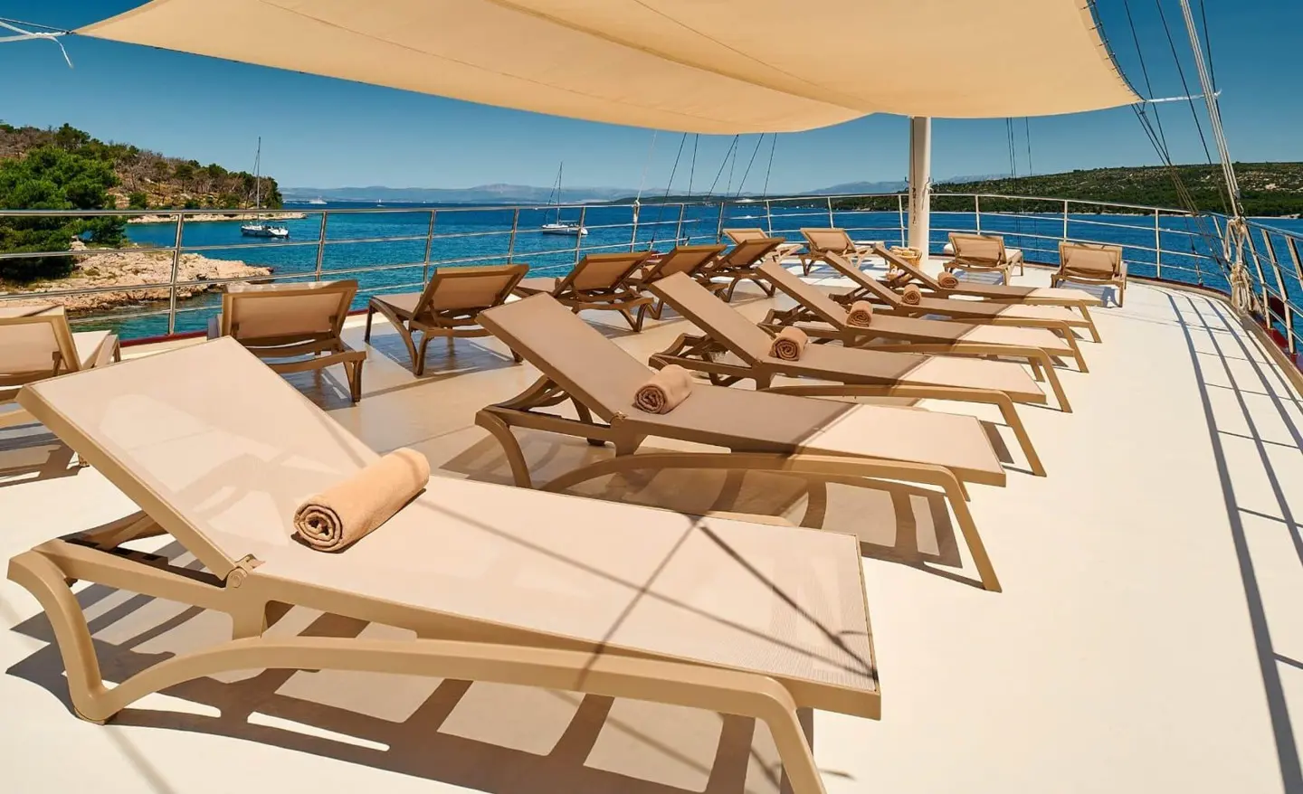 Luna yacht deck with row of beige sun loungers under shade, sea in background