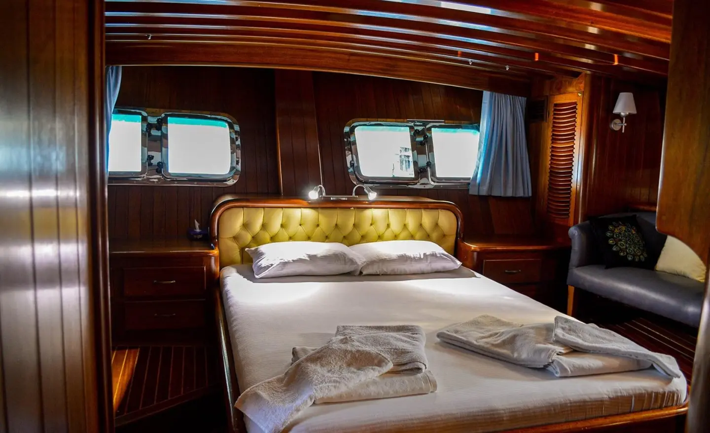 Cruise ship cabin interior with made bed, wooden walls, and towels on pillows