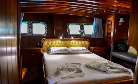 Cruise ship cabin interior with made bed, wooden walls, and towels on pillows
