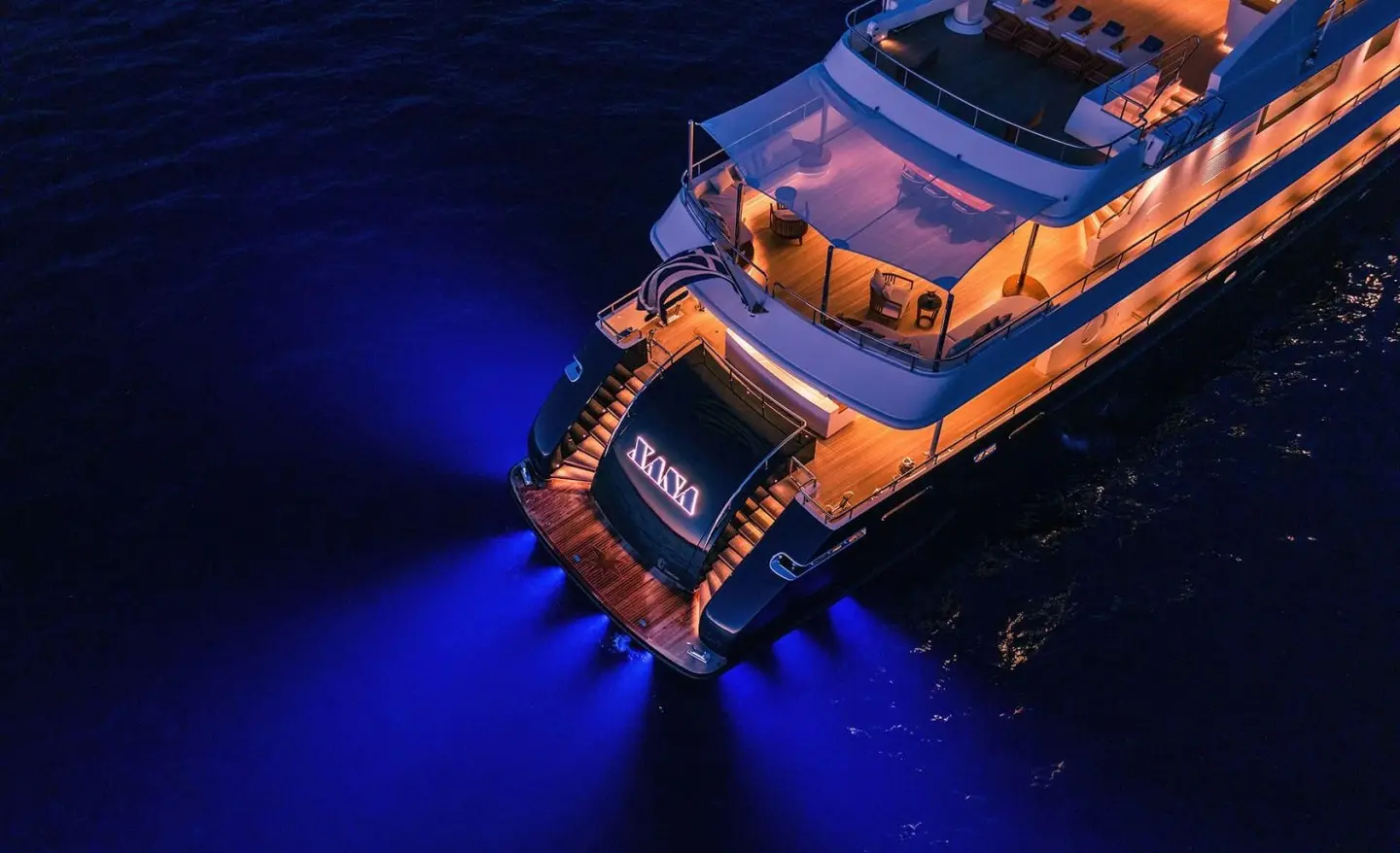 Xana luxury yacht at sea, illuminated blue under dark sky, aerial view