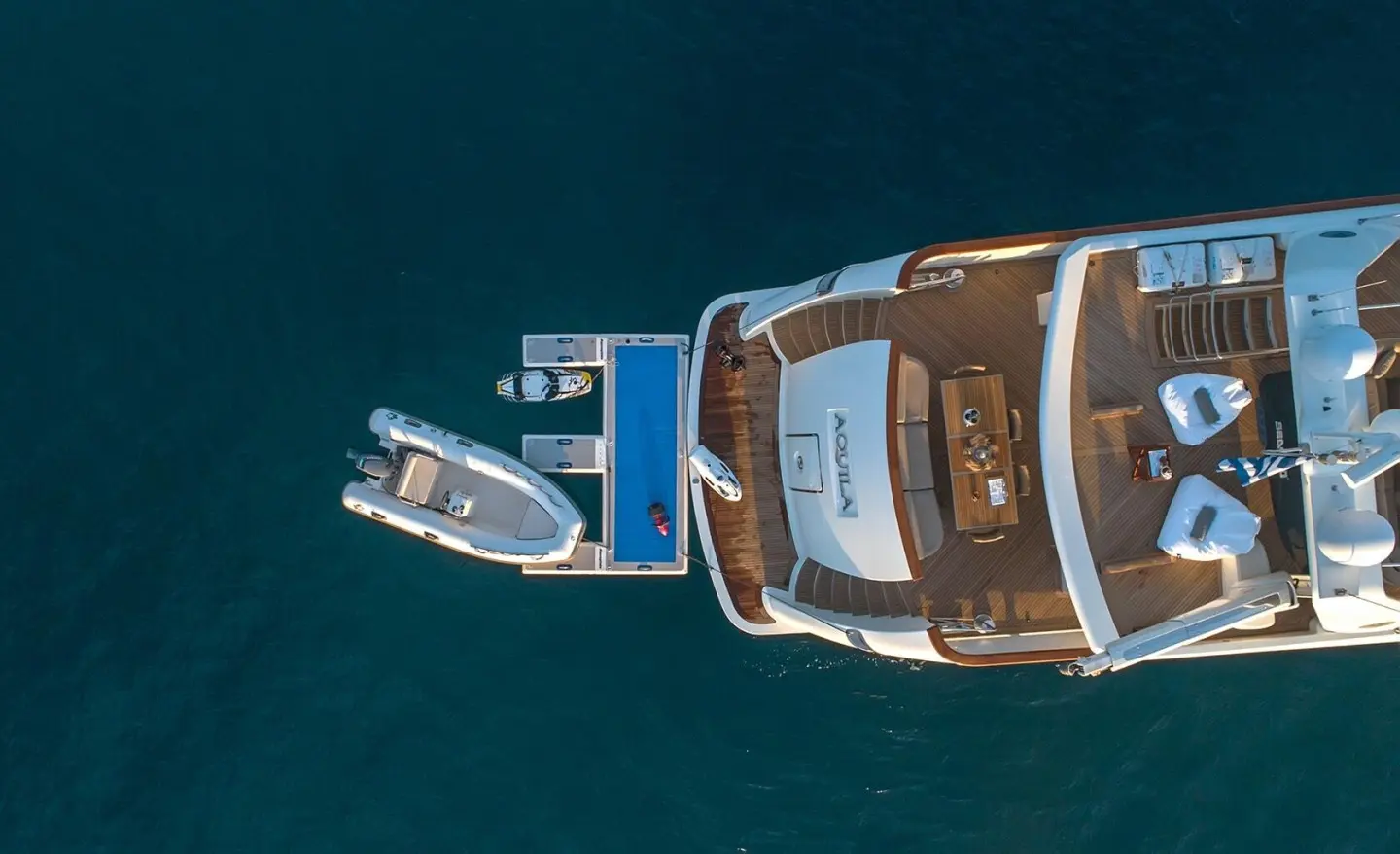 Top-down view of luxury Aquila yacht at anchor with deck seating and blue water