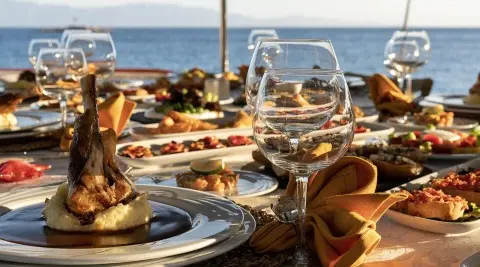 Arif Kaptan A dining deck with wine glasses and plated gourmet dishes on a seaside table