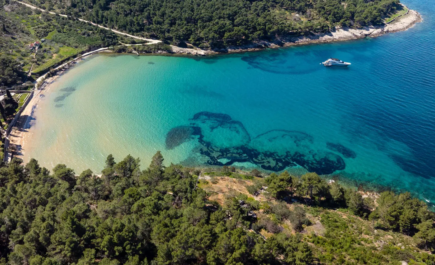 Phantom luxury yacht anchored near turquoise bay with forested coastline at sunset