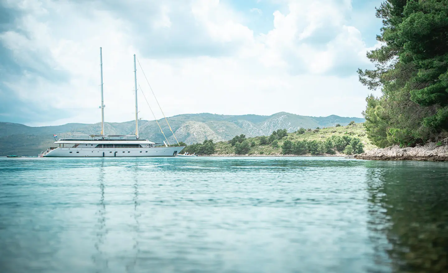 Anima Maris yacht anchored near a calm shoreline with hills in the distance