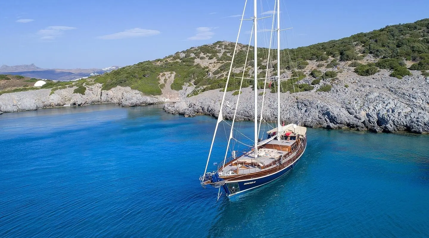 Zephyria II gulet anchored in calm blue water with rocky coastline in the background