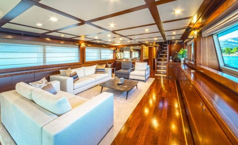 Interior lounge of Seventh Sense yacht with cream sofas, wooden panels, and large windows showing water and shore