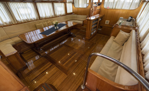 Interior of a luxurious wooden yacht with a long table, cream sofas, and windows around