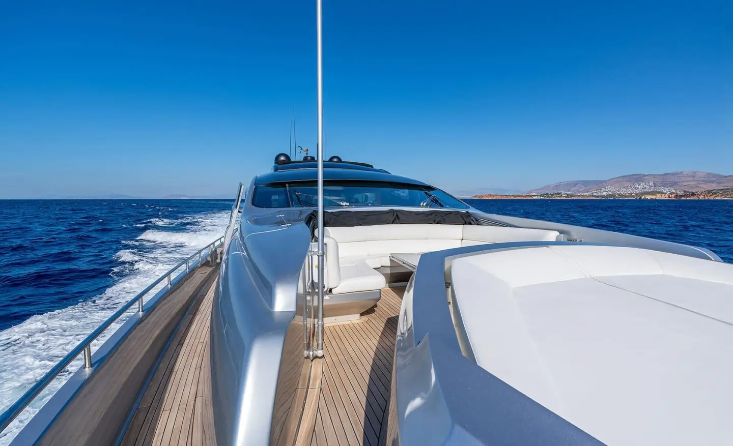 Foredeck of a yacht named One with teak rails and blue water background