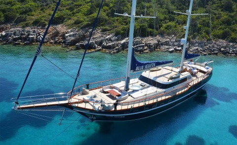 Blue Heaven sailing yacht anchored near rocky coastline with turquoise waters