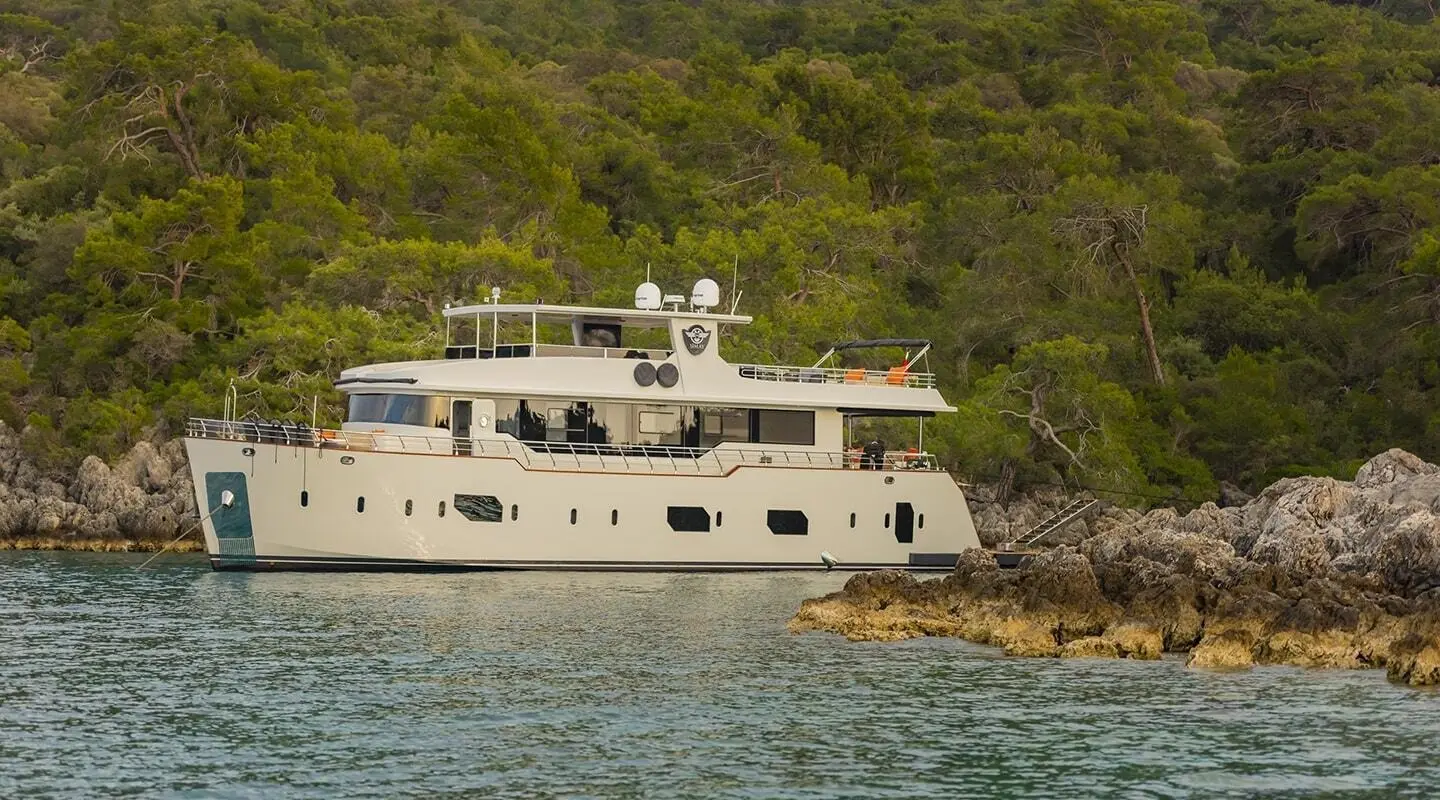 Simay M luxury motor yacht anchored near rocky coastline with green pine trees