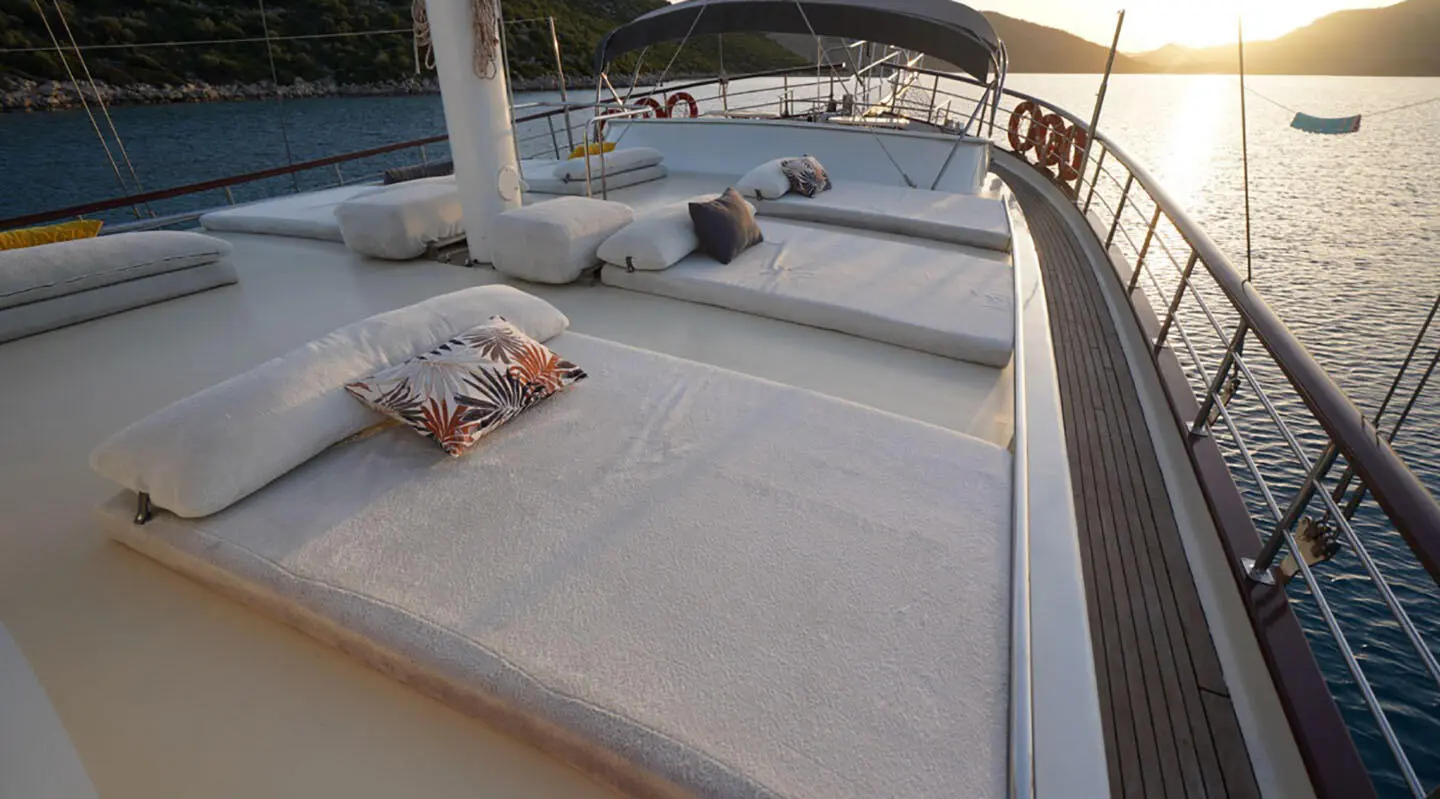 White sunbathing cushions with patterned pillows on a yacht deck at sunset
