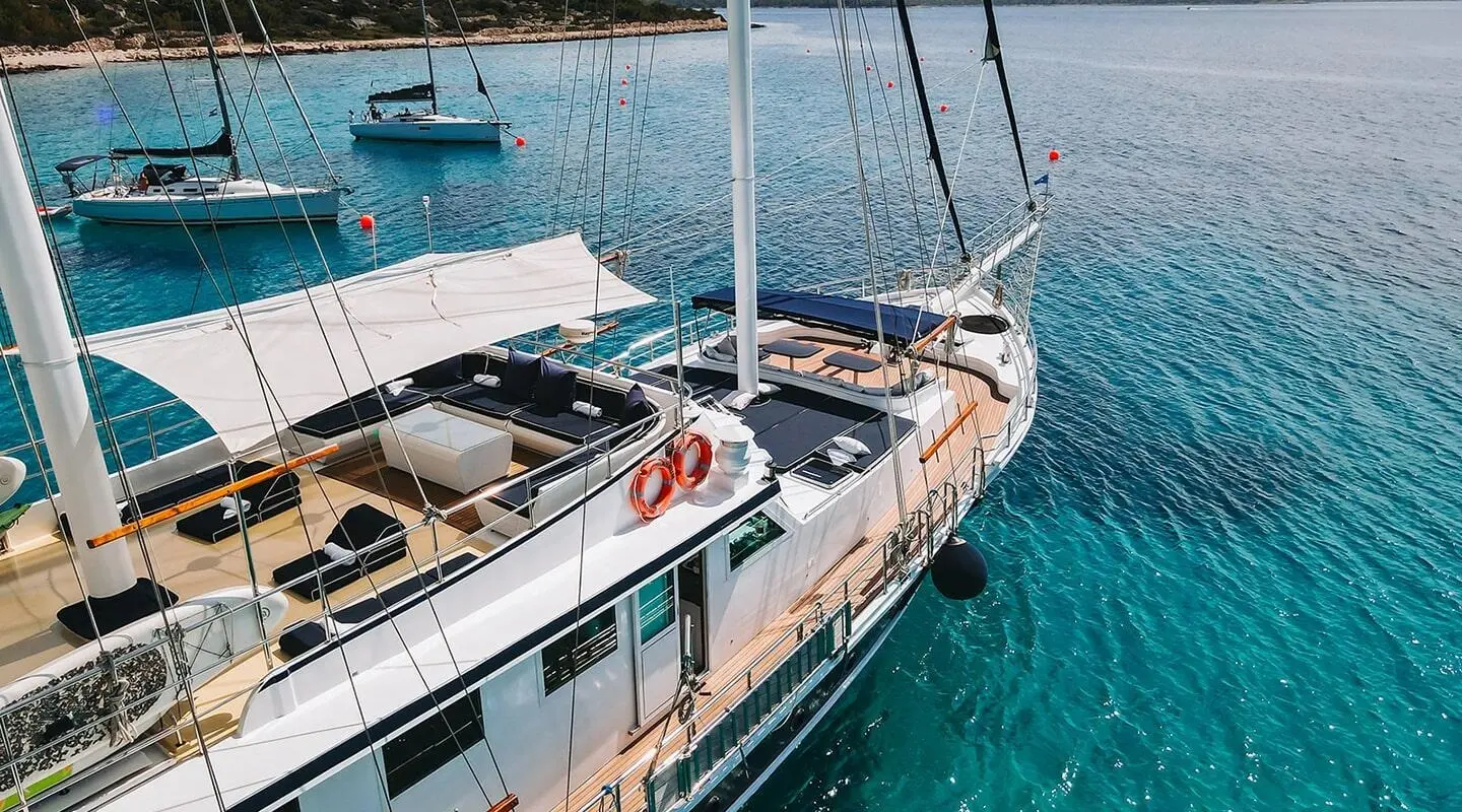 A white luxury gulet named Aurum docked at sunset with wooden deck and sails