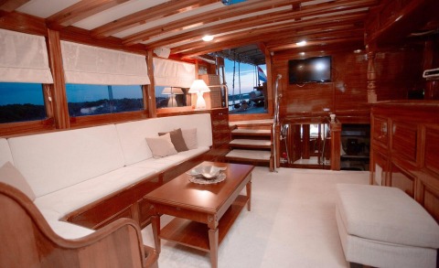 Interior with wooden decor, white cushioned sofa, coffee table; stairs and outdoor deck visible through windows