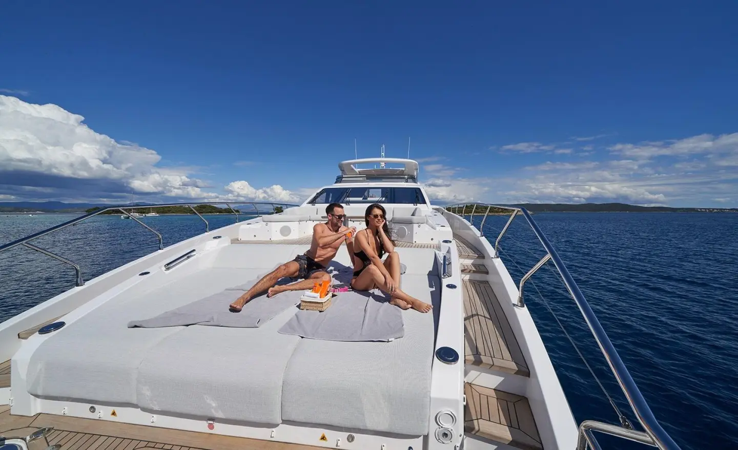 Couple lounging on a white yacht deck with the bow and sea visible