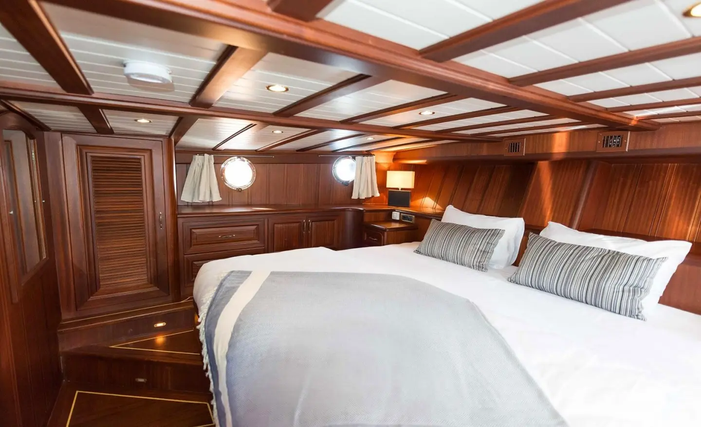 Wood-paneled bedroom aboard with a double bed and grey striped pillows