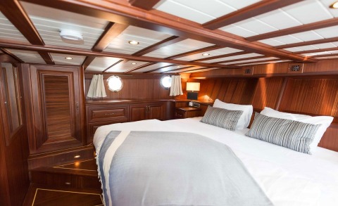 Wood-paneled bedroom aboard with a double bed and grey striped pillows