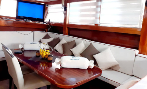 Gulet Gardelin saloon with wooden table and cushioned seating, blankets and coffee cups in the foreground