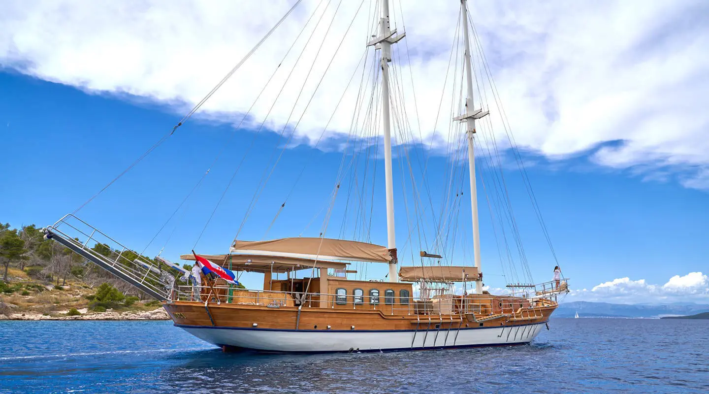 Wooden sailing yacht Libra on blue sea under clear sky with shore in background