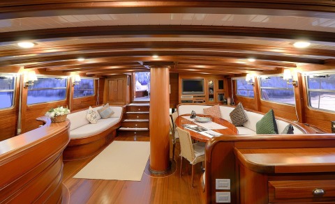 Inside saloon with wood paneling and seating, round table, TV, shelves; warm lighting and staircase in the background