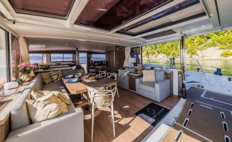 Luxurious yacht interior with dining table, light sofas, chairs, flowers and large windows overlooking a coastal view