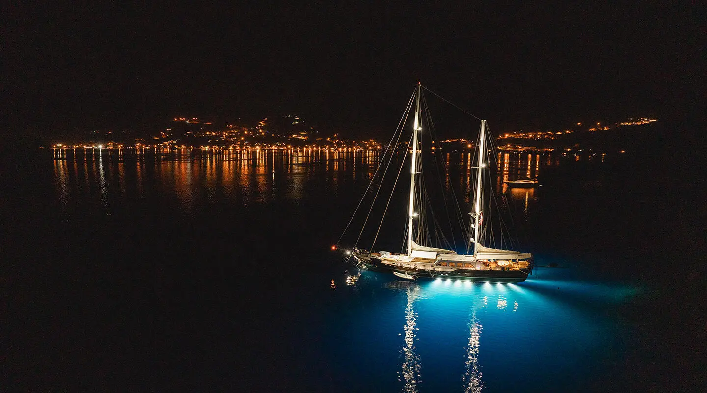 Yacht La Bella Vita moored at night with lit reflection on calm water