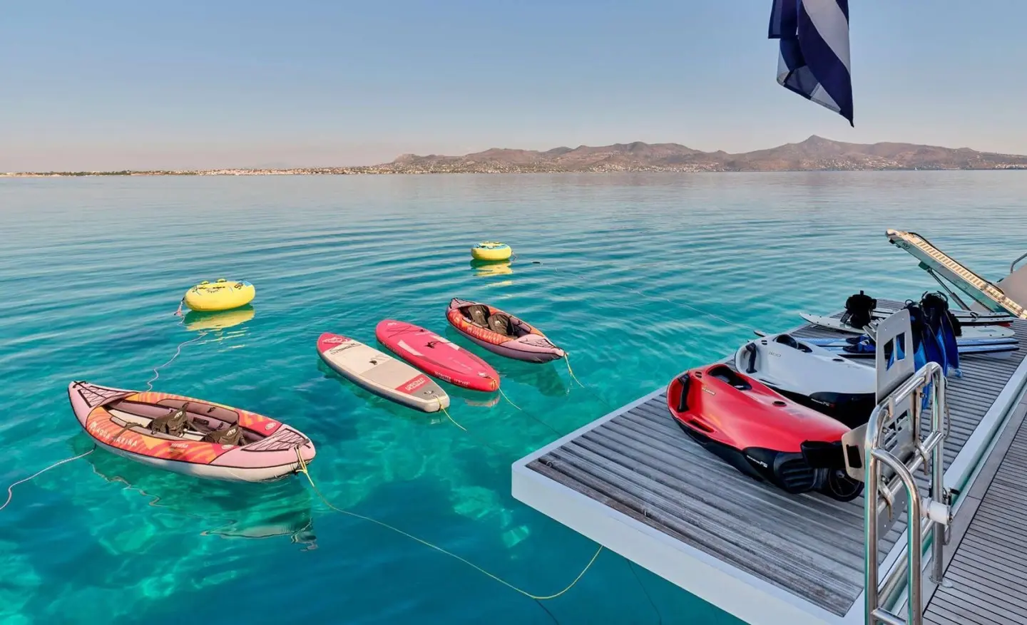 Christal Mio yacht masts and a platform with colorful inflatables on turquoise water