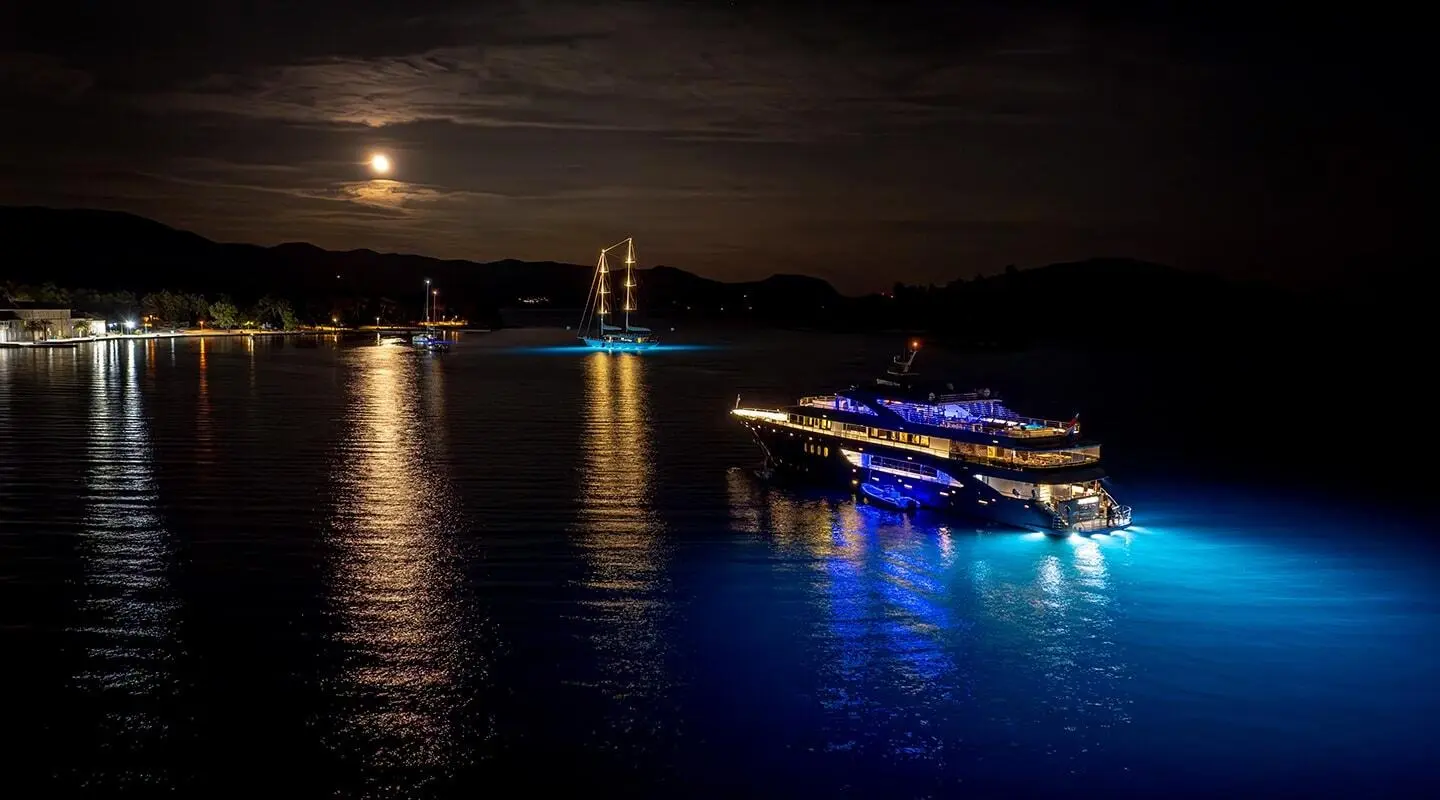 Yacht Freedom illuminated at night with blue lights on calm water