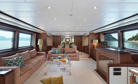 Interior of a luxury motoryacht Idylle with brown upholstered seating, glass coffee table, and large windows showing sea view