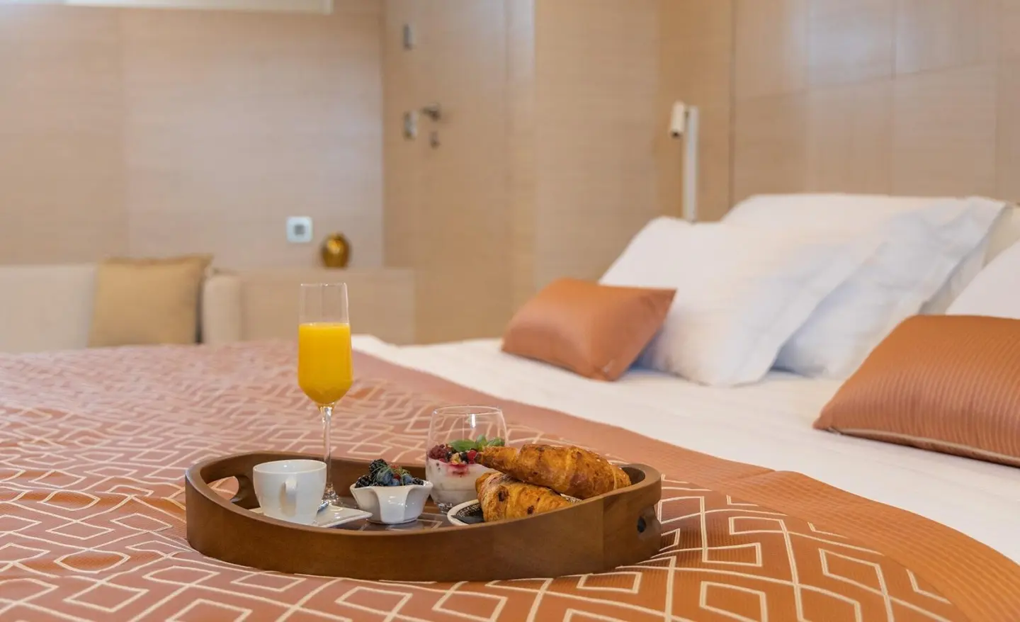Sunlit yacht interior with brown patterned floor, bed, pillows, and orange juice on a tray