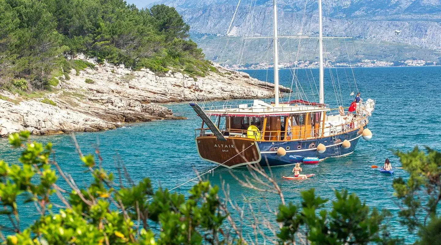 Yacht named Altair anchored near rocky coastline with blue water