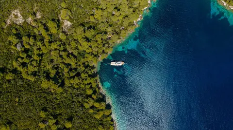 Eleganza yacht anchored near lush green coastline with calm blue water at sunset