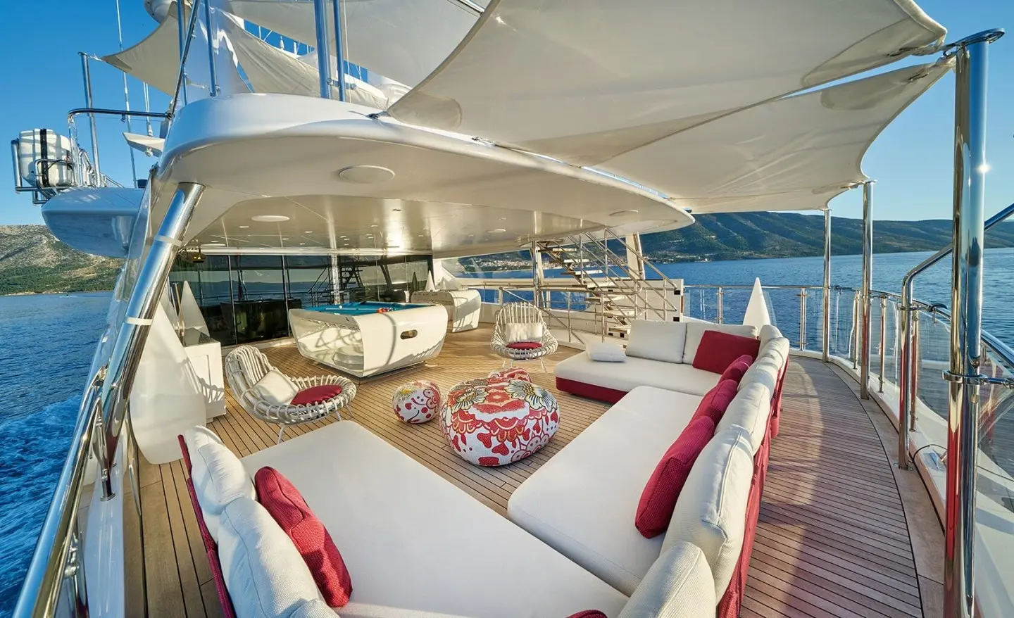 Deck scene on Happy Me yacht with white seating and red pillows overlooking blue sea
