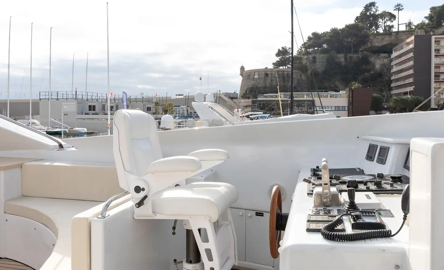 On the yacht deck with white chairs and a helm, overlooking calm water