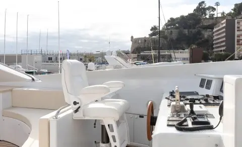On the yacht deck with white chairs and a helm, overlooking calm water