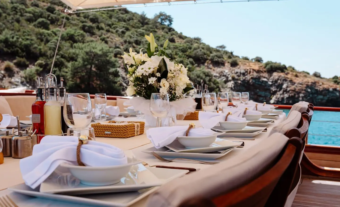 Table setting on a gulet with cushions and rocky coastline in background