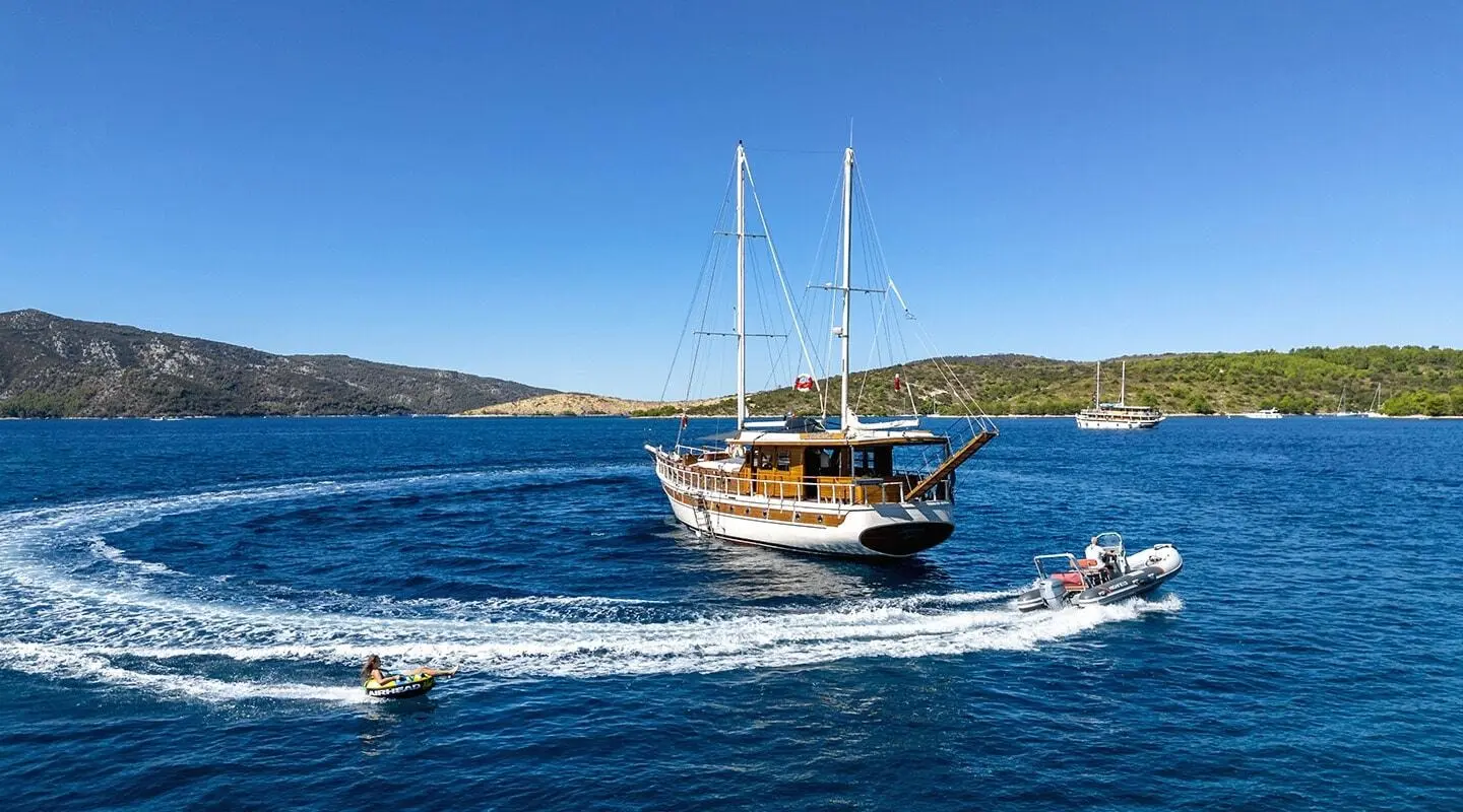 Aborda yacht sailing near rocky coastline at sunset with blue sea
